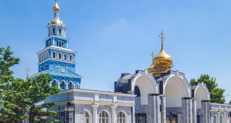 Blue-and-white Russian Orthodox church with golden onion domes set against a clear sky.