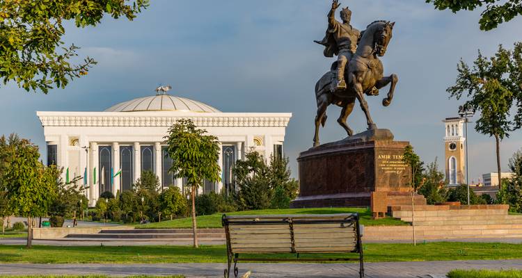 Statue of Amir Timur on horseback facing Uzbekistan Senate building in a landscaped city park.