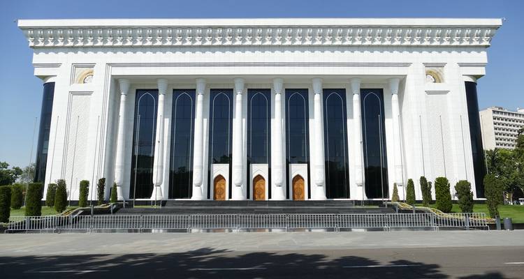 A grand white neoclassical government building with tall columns and reflective windows under a clear blue sky.