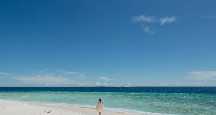 Femme marchant sur un sable blanc immaculé avec un océan turquoise éclatant et bleu profond sous un ciel dégagé