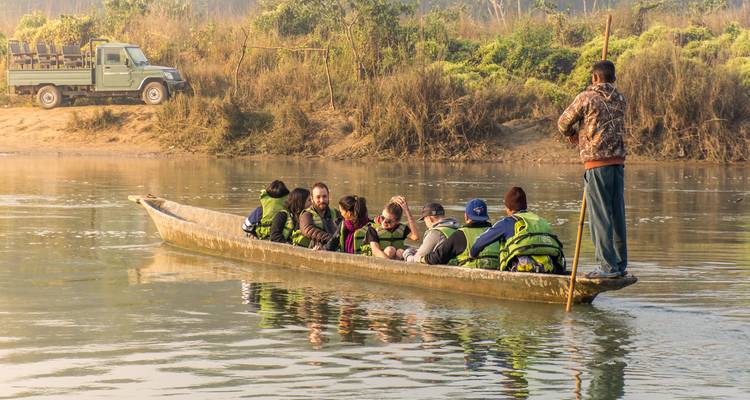 Les touristes vêtus de gilets de sauvetage naviguent en pirogue creusée sur une rivière calme tandis qu'un guide pousse l'embarcation à la perche depuis l'arrière.