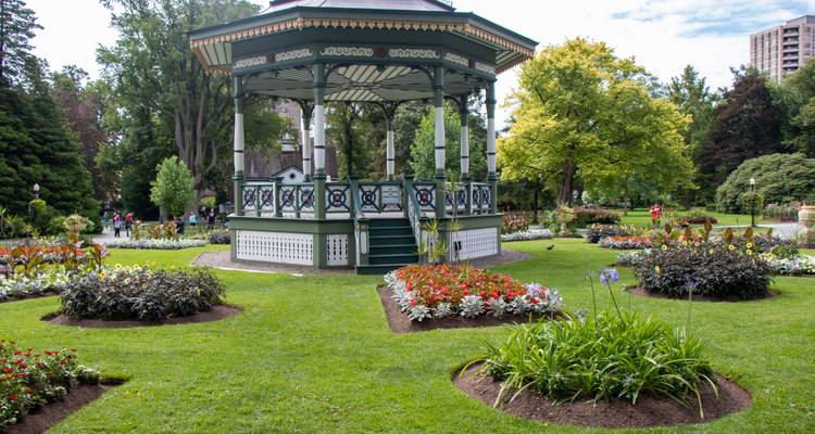 Kiosque à musique victorien entouré de parterres de fleurs colorés dans un jardin public bien entretenu.