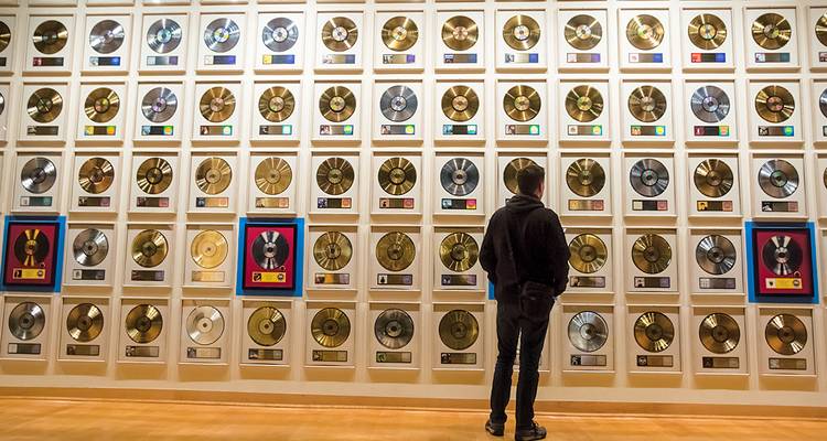 Un visiteur se tient devant un immense mur de disques d'or et de platine encadrés dans un musée de la musique.