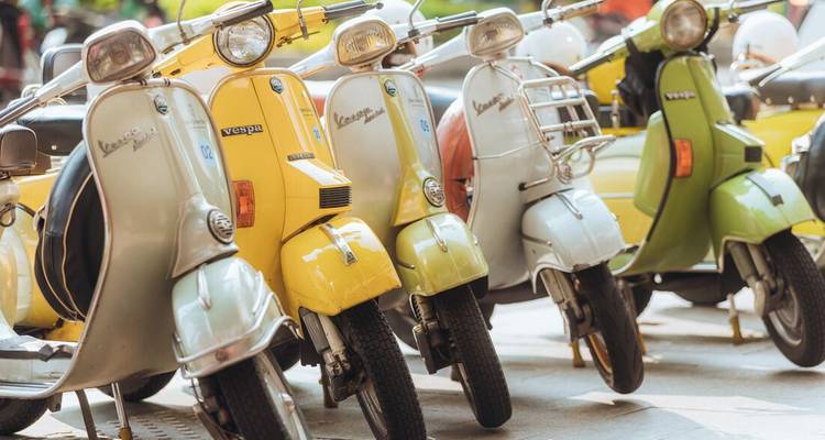 Line of vintage Vespa scooters in pastel colours parked side by side.