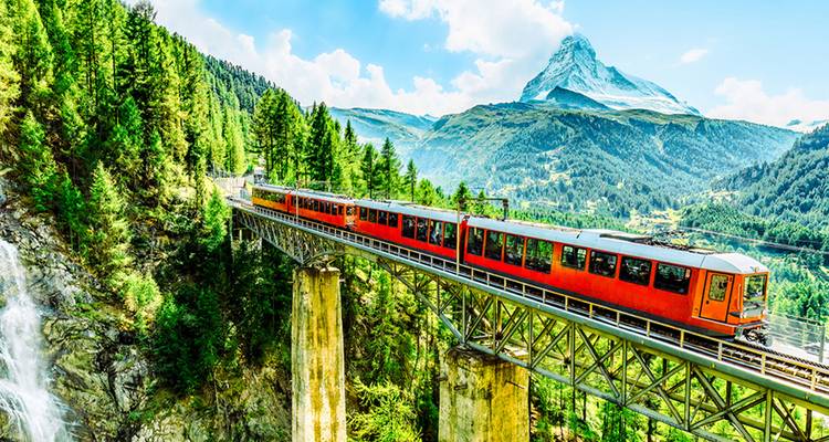 Tren rojo brillante de engranajes cruzando un puente alto con el nevado Matterhorn elevándose detrás.