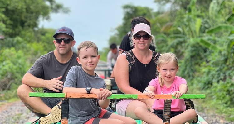 Family enjoying a ride on Battambang’s bamboo train through lush countryside.