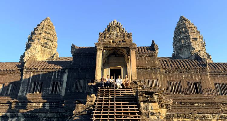 Travelers gathered on the grand staircase of Angkor Wat’s central sanctuary under a clear blue sky.