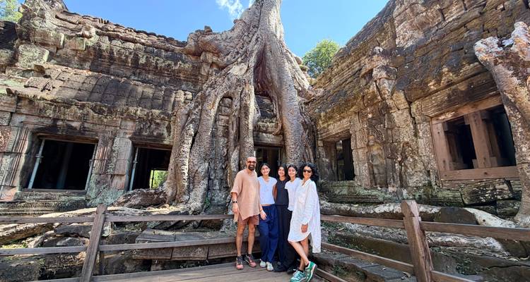 Friends posing beside massive tree roots enveloping a temple wall at Ta Prohm.