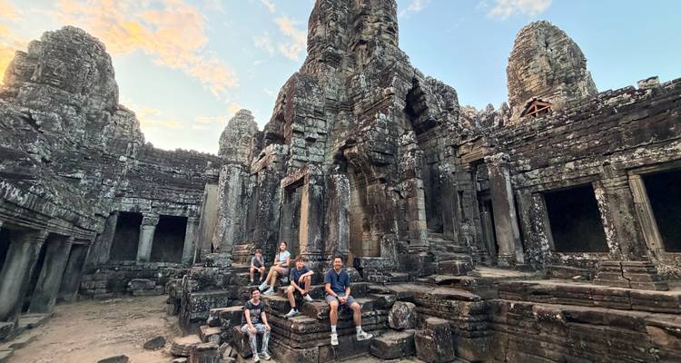 Group seated among towering stone faces and ruins at Bayon Temple during late afternoon.