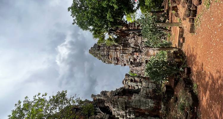 Weathered stone tower of a remote Cambodian temple framed by dramatic storm clouds and red earth.