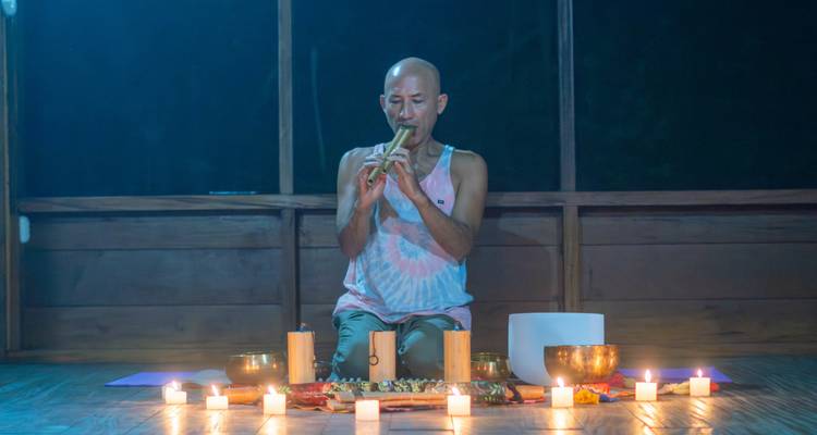 Un homme jouant de la flûte en bambou lors d'une cérémonie en soirée à la lumière des chandelles, à côté de bols chantants et de cristaux.