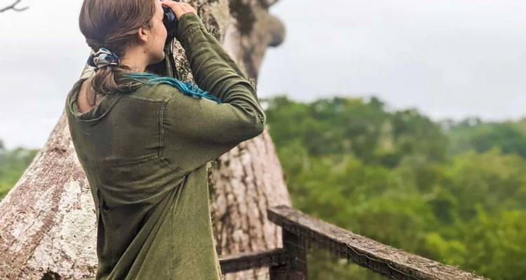 Una mujer escanea el dosel de la jungla con binoculares desde una plataforma de madera.