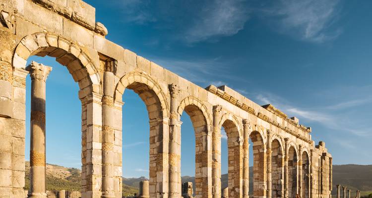 Longue rangée d'arcs romains antiques de Volubilis illuminés par la lumière chaude du soir.