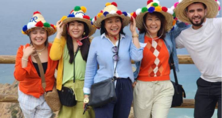 Groupe de touristes portant des chapeaux de paille colorés à pompons qui sourient avec des falaises océaniques en arrière-plan.