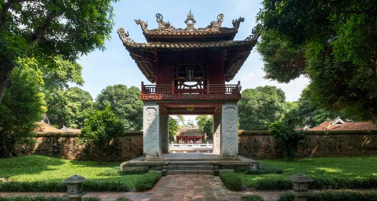 Pavillon en bois ouvragé avec une cloche en bronze se dresse au bout d'une allée en pierre dans un jardin de temple paisible.