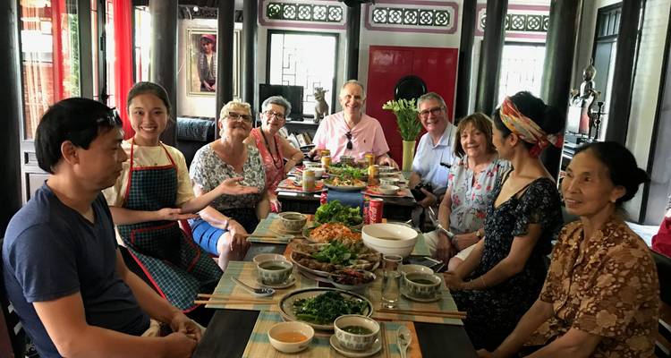 Des voyageurs souriants se rassemblent autour d'une longue table chargée de plats vietnamiens à l'intérieur d'une maison traditionnelle.