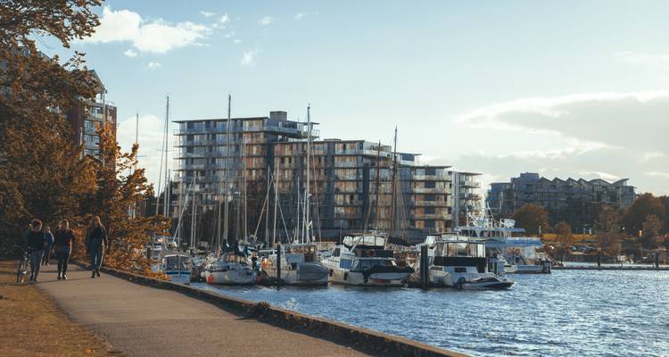 Waterfront promenade met voetgangers, zeilboten en moderne appartementen op een rustige middag