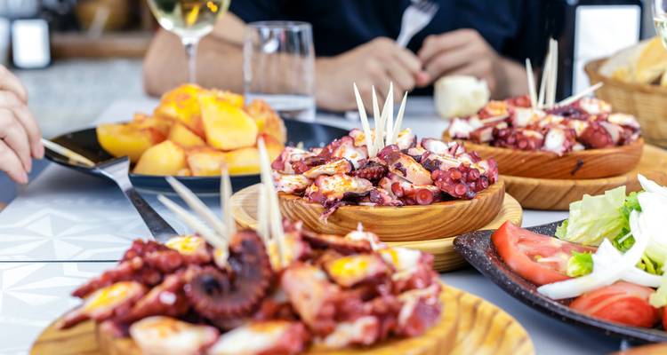 Mesa cargada de platos de pulpo, papas y vino durante una comida portuguesa relajada