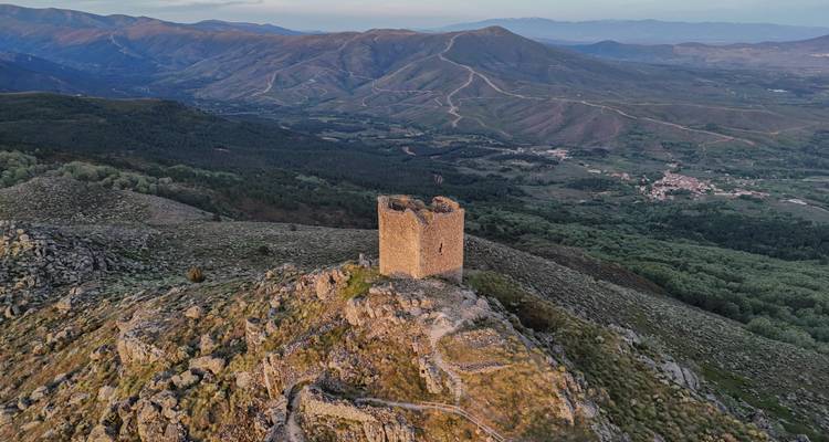 Vista aérea con dron de una solitaria torre medieval de vigilancia encaramada en una cresta escarpada con un impresionante telón de fondo montañoso