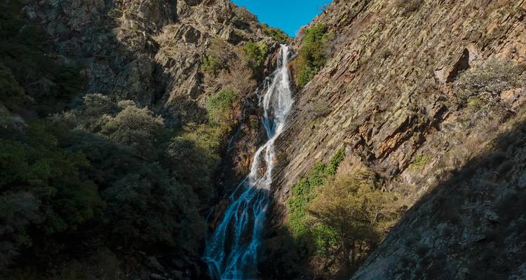 Una cascada alta y esbelta cayendo por un acantilado rocoso empinado hacia la sombra