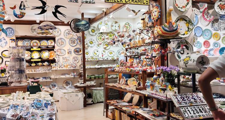 Boutique de céramiques grecques colorées remplie d'assiettes, de figurines et de souvenirs, avec un acheteur en bordure du cadre.