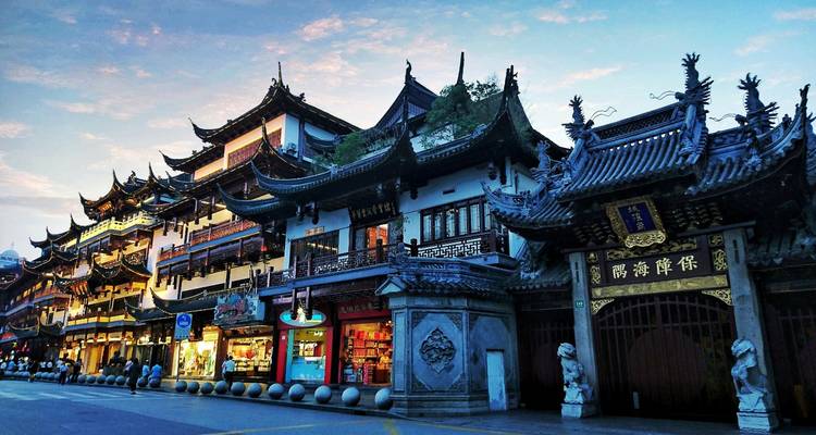 Traditionelle chinesische Gebäude mit kunstvollen Dächern, die in der Dämmerung entlang einer Fußgängerzone beleuchtet sind.