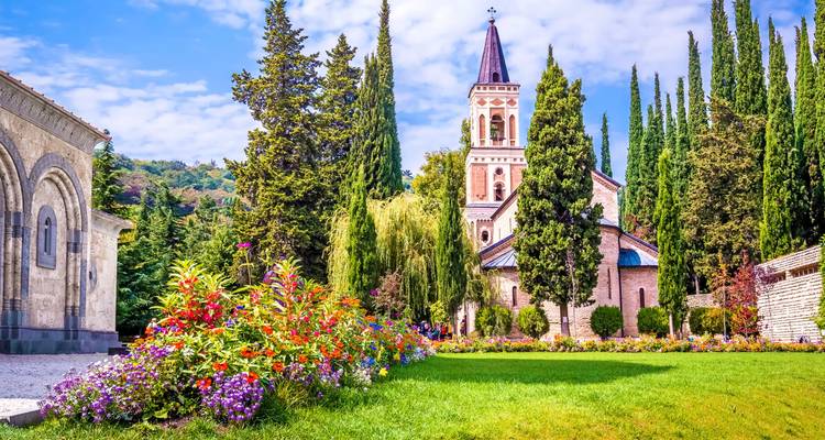 Jardin de fleurs colorées et haute tour de cloche d'un monastère se dressant contre le ciel bleu en Kakhétie