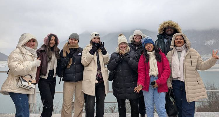 Groupe de touristes vêtus de manteaux d'hiver posant à côté d'un lac enneigé et de montagnes brumeuses