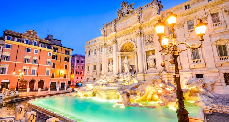 Evening lights illuminate the turquoise waters and ornate sculptures of Rome’s Trevi Fountain.