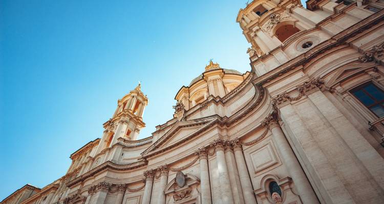 Upward angle of ornate baroque church façade and twin towers gleaming against a clear blue sky.