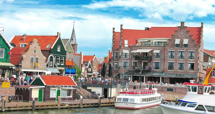 Escena animada en el paseo marítimo de Volendam con edificios holandeses tradicionales y barcas de turismo.