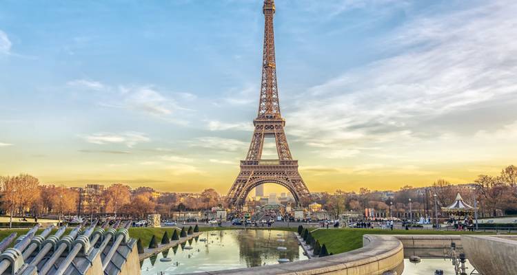 La Tour Eiffel s'élevant au-dessus des fontaines et des bassins de réflexion lors d'un coucher de soleil doré.