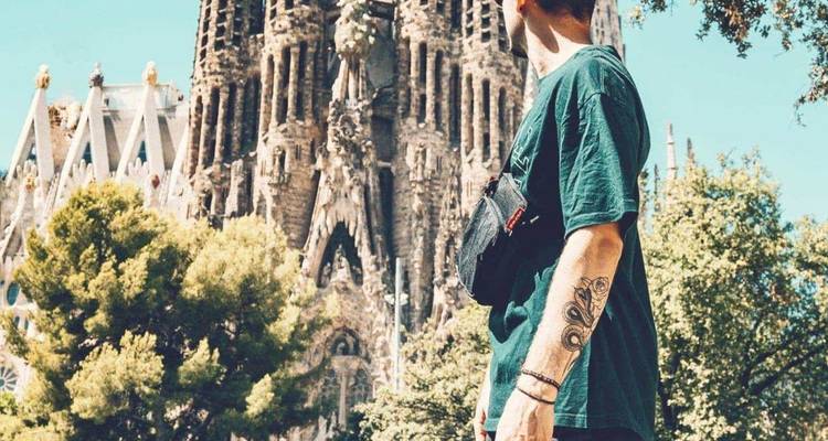Gros plan d'un touriste admirant la Sagrada Familia de Barcelone avec des arbres encadrant la basilique.