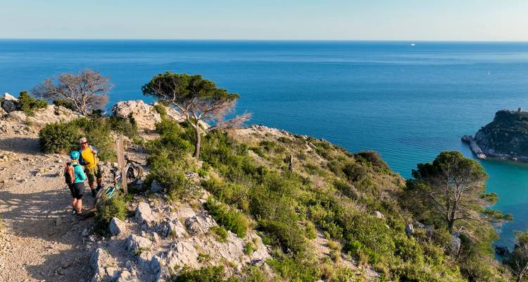 Des randonneurs se reposant sur une falaise rocheuse méditerranéenne offrant une vue panoramique sur l'océan.