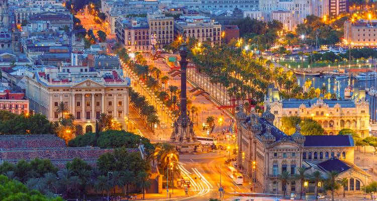 Vue aérienne nocturne du boulevard bordé d'arbres de Barcelone, centrée sur le Monument Colomb avec des lumières urbaines vibrantes.