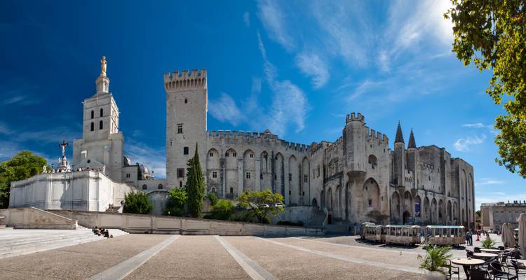 Breed pleinzicht op het imposante Palais des Papes complex onder een diepblauwe hemel.