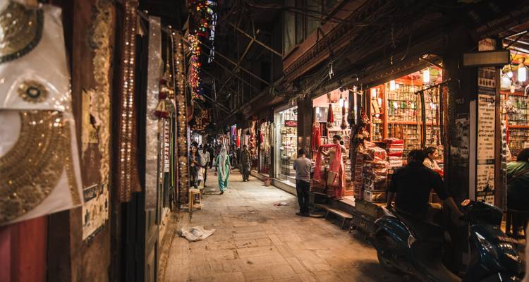 Ruelle de marché étroite illuminée par les lumières chaleureuses des boutiques, bordée de marchandises colorées et de piétons qui font du shopping en soirée.