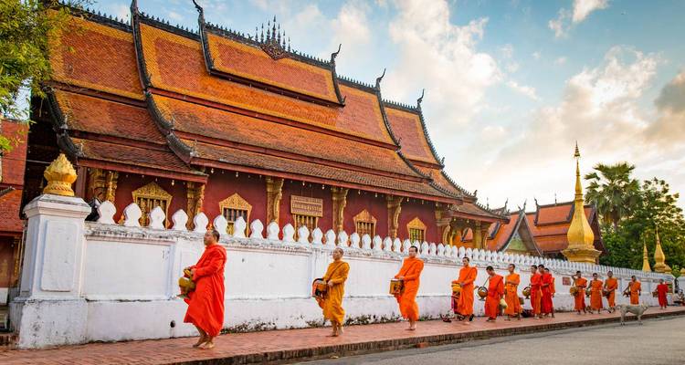 Une file de moines vêtus de robes safran passe devant les murs de temple rouges ornementés lors de la collecte matinale des aumônes.
