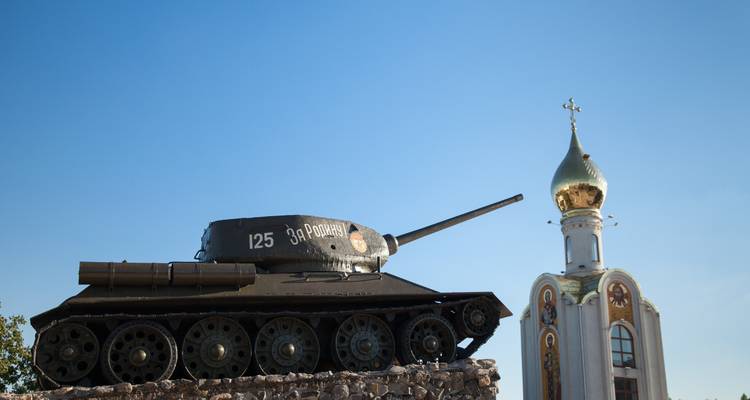 Historisch Sovjet T-34 tankmonument naast een goudkoepelkerk onder een heldere blauwe hemel.
