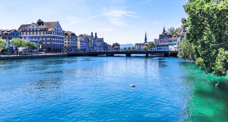 Helder blauwe rivier de Limmat die door het historische centrum van Zurich stroomt onder een felblauwe lucht.