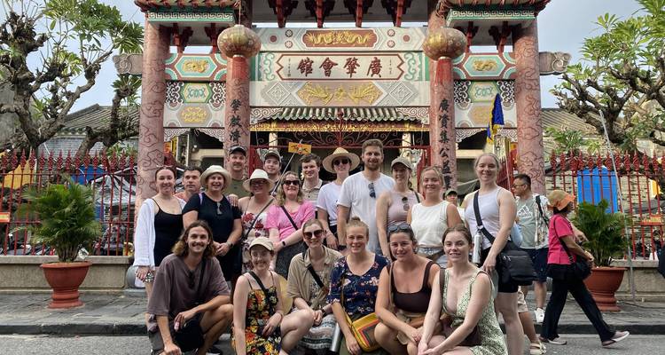 Grupo de turismo posando felizmente ante la puerta del ornamentado Salón de Asambleas Chino en Hoi An.