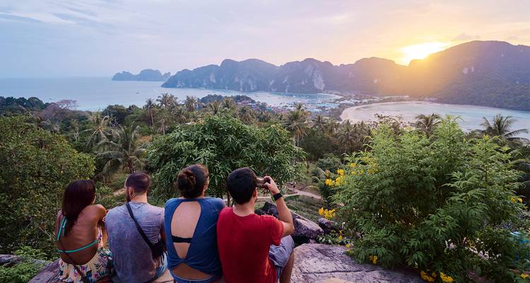 Un groupe de routards assis sur un point de vue rocheux regardant le coucher de soleil sur les îles Phi Phi et les deux baies.