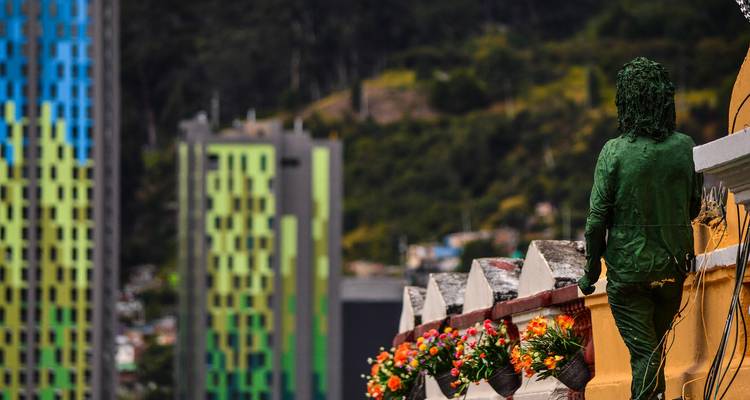 Estatua pintada de verde que domina los coloridos departamentos modernos de gran altura de Bogotá con las montañas de fondo.
