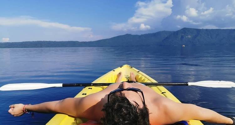 Reiziger die ontspant op een gele kayak in kalme kratersmeermeren onder dramatische lucht.