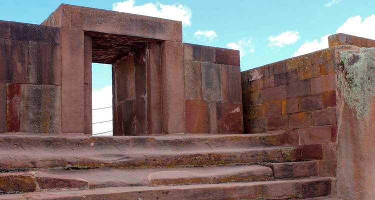 Des marches en pierre mènent vers l'entrée sculptée d'une ruine ancienne de Tiwanaku se dressant contre un ciel bleu.