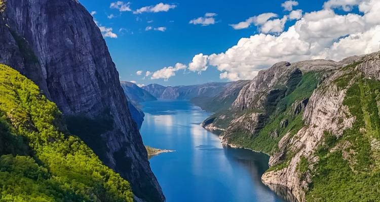 Ein dramatischer norwegischer Fjord mit steilen Granitfelsen und einer ruhigen blauen Wasserstraße, die sich in die Ferne erstreckt.