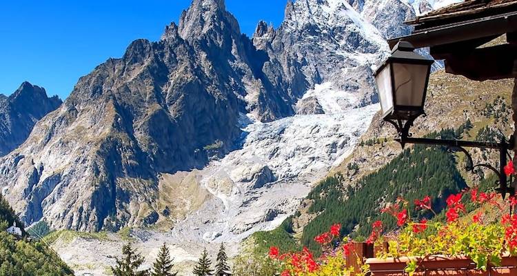 Dramatic view of jagged alpine peaks and glacier from a flower-adorned balcony.