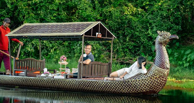 Elegant peacock-shaped wooden boat gliding on calm water with smiling guests and a rower.