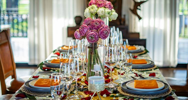 Luxuriously set dining table with pink lotus centerpieces and neatly arranged glassware indoors.