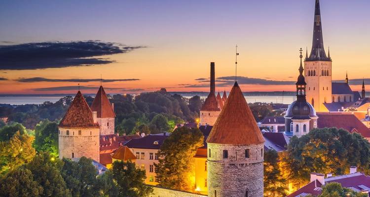 Abendliche Aussicht auf Tallinns mittelalterliche Steintürme und Mauern, die sich gegen einen farbenfrohen Sonnenuntergangshimmel abzeichnen.